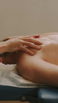 close vertical view of therapist hands pressing fingers across upper back and shoulder during spa massage