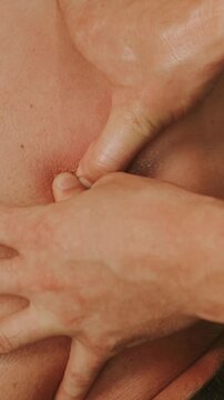 vertical close-up of therapist hands massaging upper back and shoulder, thumbs pressing muscle knots with glow