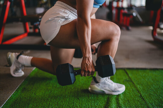 Close up of Hispanic female hand gripping heavy dumbbell during lunge exercise, strong athletic woman training legs in gym, muscle detail, body shaping, copy space.