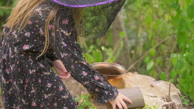 child hand stirring copper cauldron with stick, natural ingredients, water with leaves and berries inside, Halloween or fantasy witch crafting setup, Esoteric practice herbal medicine and magic potion
