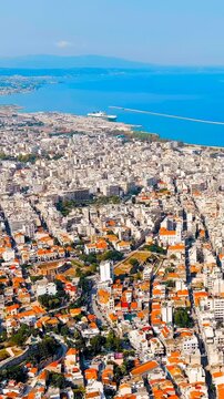 Vertical video. Patras, Greece. Drone footage over the dense city center and historic medieval fortress, terracotta rooftops spreading toward the deep blue Gulf of Patras under bright summer sun. Dro