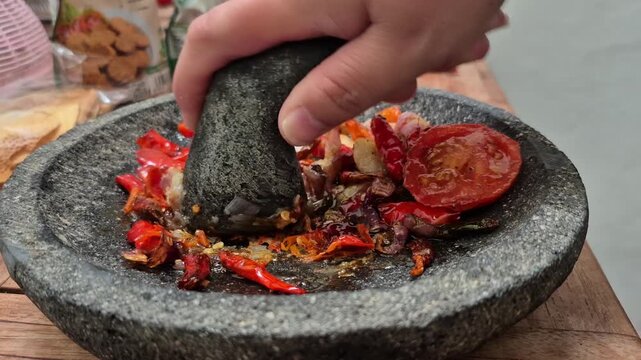 The process of grinding ingredients for cooked shrimp paste sambal (or tomato sambal) using a traditional stone mortar 