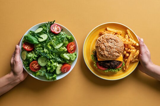Hands holding healthy salad and unhealthy burger with fries