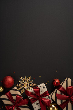 Merry Christmas and Happy New Year greeting with wrapped gifts, red ornaments and gold snowflake on black vertical background
