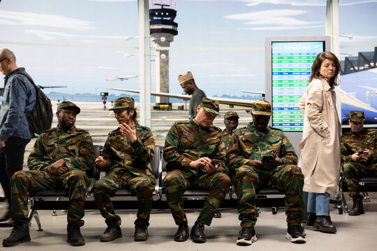 Army soldiers in airport use phone to tell family about arriving late home for holidays, officers in departure terminal use smartphone to text relatives about homecoming after finishing military duty.