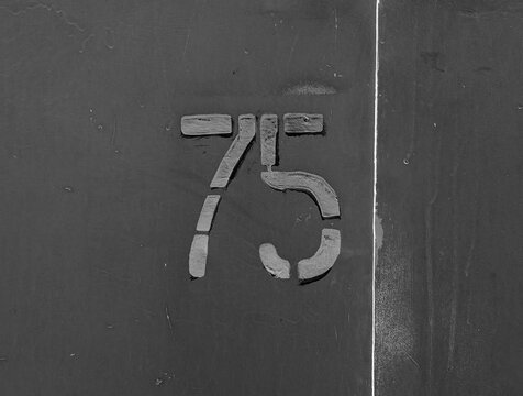 Gray number 75 on garage door in retro style. Digits on a textured metal surface with weathered details