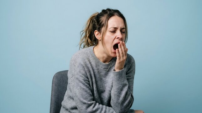 Tired adult woman yawning and showing signs of fatigue while sitting