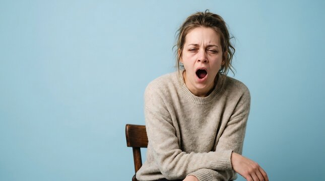 Tired woman yawning while sitting on a wooden chair against a blue
