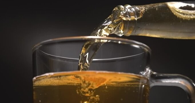 Beer pouring from glass bottle into mug in slow motion