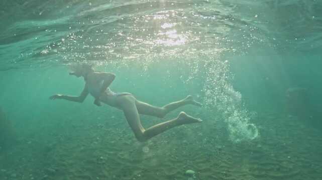 A happy girl in a mask with a snorkel is swimming underwater. Half underwater scene of little girl with diving mask and snorkel swimming in turquoise tropical sea water of exotic island. Slow motion