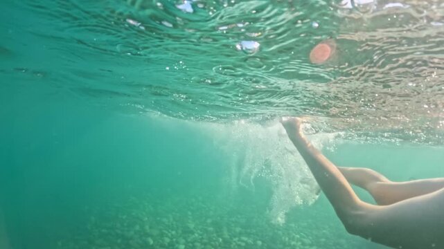 A happy girl in a mask with a snorkel is swimming underwater. Half underwater scene of little girl with diving mask and snorkel swimming in turquoise tropical sea water of exotic island. Slow motion
