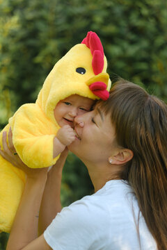 Happy mother holding cute baby in yellow chicken costume outdoors in park on sunny day