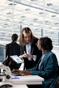 African American woman and coworker brainstorm semiconductor hardware prototypes in a microchip factory research office, collaborating on technical innovations.