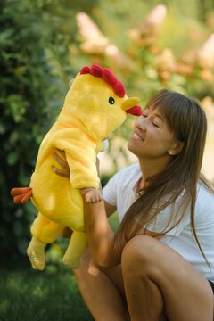Happy mother holding cute baby in yellow chicken costume outdoors in park on sunny day