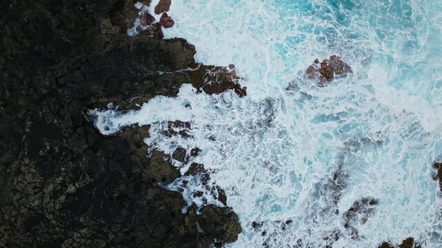 Aerial top-down view of Tenesar coastline in Lanzarote. Crashing waves, black volcanic rocks and foamy ocean patterns create a dramatic seascape.