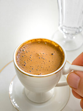 Hand Holding Handle of White Porcelain Cup Filled with Foamy Turkish Coffee