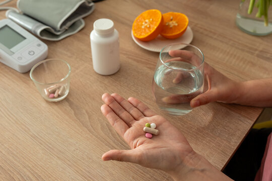 Female hand displaying mixed pills and capsule while holding water near fresh orange at home. Concept of polypharmacy, nutritional supplements, immunity care and medication management.