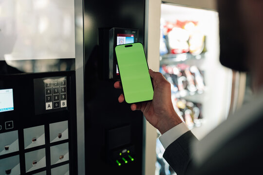 Person paying for products at vending machine using smartphone with green screen for contactless mobile payment