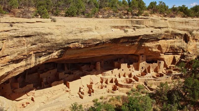 Warm sunset light illuminates ancient masonry dwellings nestled beneath towering sandstone cliffs at Mesa Verde Cliff Palace