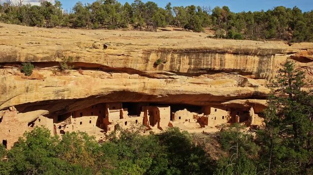 Golden sunset light bathes ancient preserved sandstone masonry structures sheltered within the giant natural alcove of Spruce Tree House
