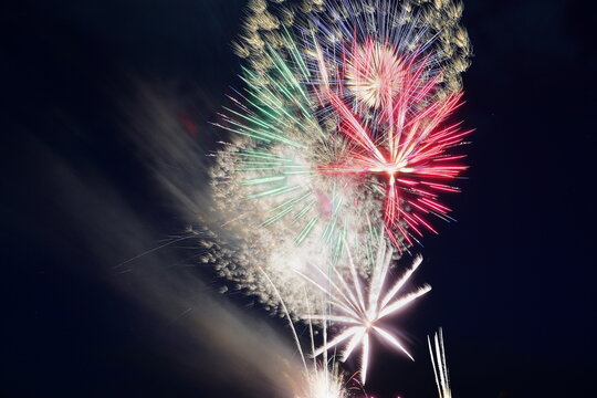 夏の夜空を鮮やかに彩る華麗な花火大会の打ち上げ風景。赤や緑、白の火花が幾重にも重なり合い、闇夜に大輪の花を咲かせる幻想的で祝祭感あふれる光の芸術。