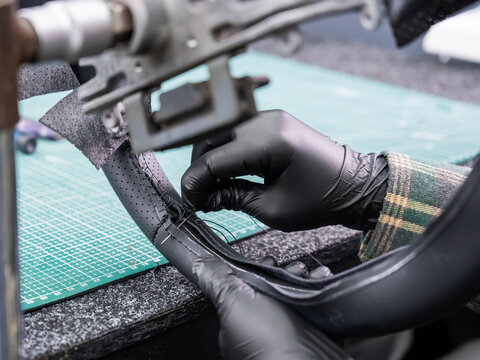 A seamstress in a workshop makes a new leather cover for a car steering wheel.