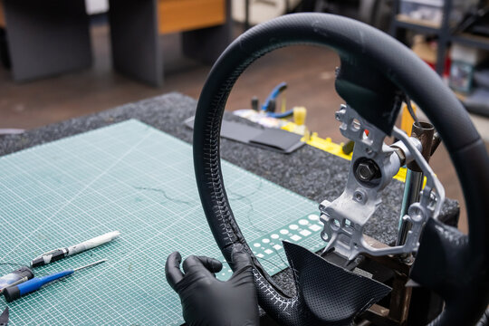 A seamstress in a workshop makes a new leather cover for a car steering wheel.