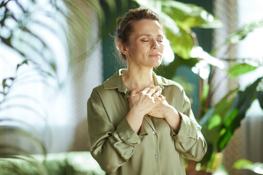 A woman finds a moment of serenity by the window, practicing mindful breathing to relieve stress and connect with her inner self in a lush home environment.