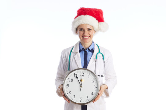 A blonde female physician in a Santa hat holds an analog clock set near midnight, highlighting emergency medical services and holiday shift work availability.