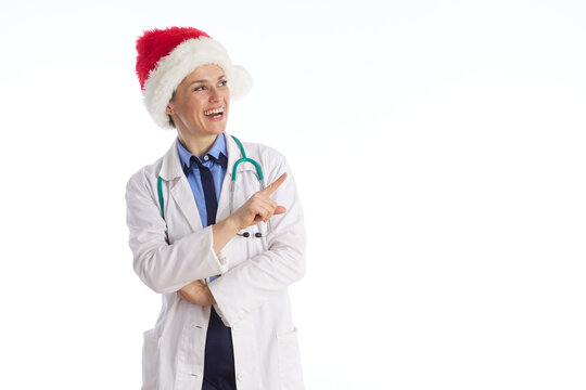A smiling female physician in a Santa hat points upward while standing with arms crossed, conveying trust and medical expertise during the Christmas season.