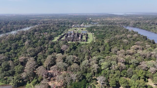 Aerial landscape view of a drone flying sideways from right to left showcasing the iconic Angkor Wat temple complex surrounded by ancient water moats and lush jungle
