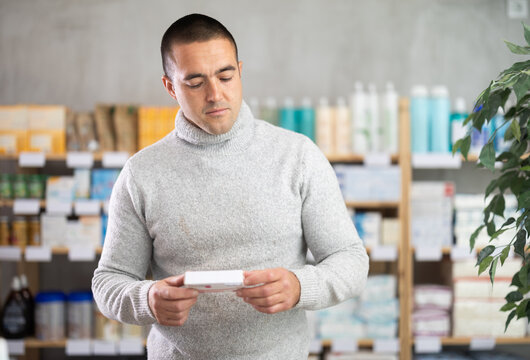Man studies composition of paracetamol pills, buys product in drug store. Checking for absence of GMOs, age restrictions and recommendations for use.