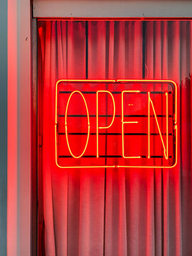 Glowing red neon open sign hanging in a window framed by curtains
