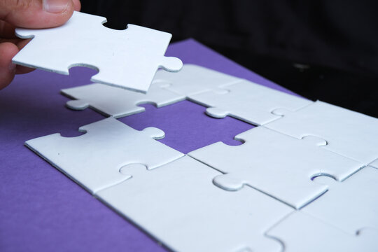 Hand pushing a puzzle piece into the gap to complete the puzzle, illustrating the concept of integration or business merger