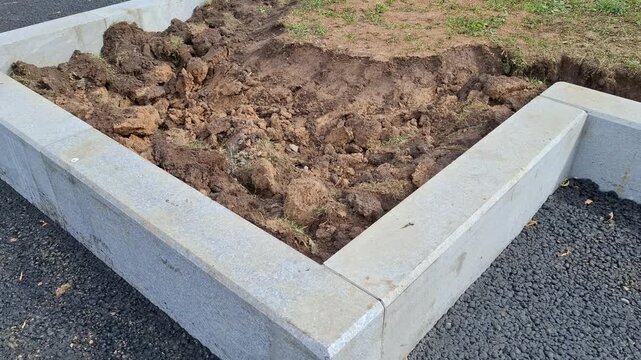 Unfinished concrete garden bed frame surrounded by new asphalt and loose soil. landscaping work, public park construction, garden preparation. New curbs along the pedestrian path