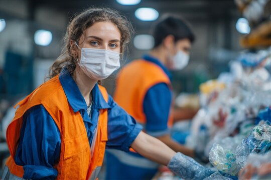 Young woman sorts recyclable materials with colleague at workstation in busy facility