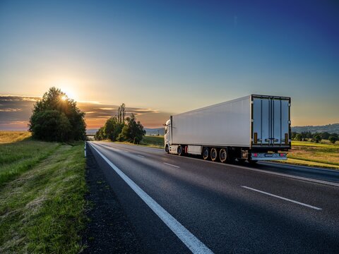 White truck driving on asphalt road in rural landscape at sunset