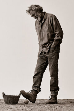 Sepia portrait of smiling senior man nudging an apple with boot