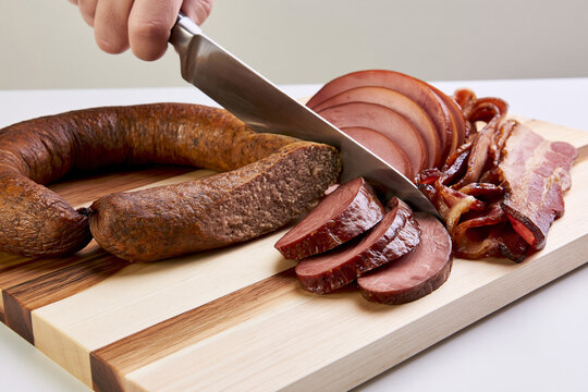 Hand slicing smoked meat beside sausage on wooden cutting board