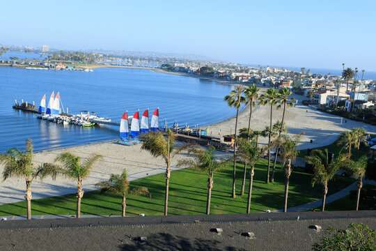 Elevated view of Mission Bay coast with small catamarans parked by a sandy beach lined with tall palm trees, San Diego, California