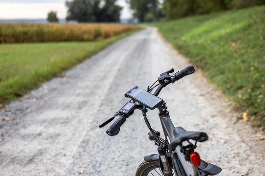 Close-up of an e-bike handlebar with GPS smartphone mount on a gravel path during a cycling trip in rural countryside.