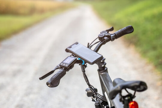 Close-up of an e-bike handlebar with GPS smartphone mount on a gravel path during a cycling trip in rural countryside.