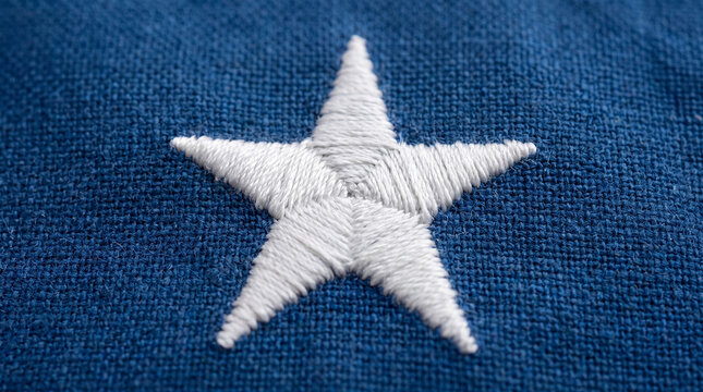 Embroidered five pointed white star on a textured blue fabric, creating a patriotic background for themes of national pride, achievement, quality, and traditional craftsmanship