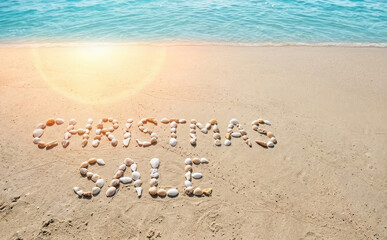 Fototapeta premium Christmas sale written with seashells on a tropical sandy beach with ocean waves for a tropical holiday shopping concept background