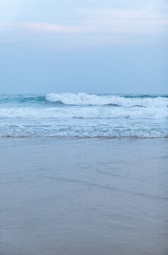Gentle sea waves lap against wet sandy beach under pale blue sky