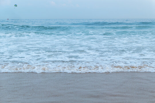 Gentle sea waves lap against wet sandy beach under pale blue sky