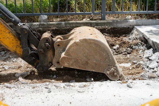 Excavator bucket digging broken concrete and soil at construction site
