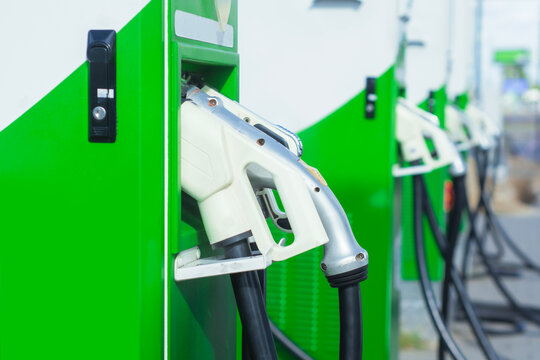 Electric vehicle charging connector at a modern EV charging station with multiple green charging units in the background. Electric mobility infrastructure and vehicle charging equipment.