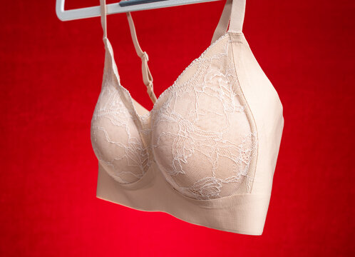 Beige floral lace bra hanging against solid red background