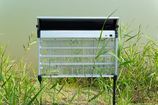 Solar insect killer lamp standing on grass in outdoor field, UV light tube with electric grid, solar panel on top